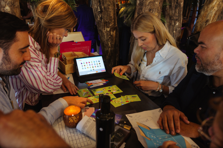 Collega’s werken samen aan een interactieve teambuildingopdracht van The Box Company met kaarten en een tablet tijdens een bedrijfsactiviteit op locatie.