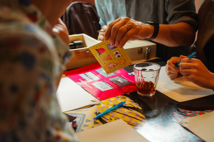 Deelnemers lossen een creatieve opdracht op tijdens een interactieve teambuildingactiviteit op locatie van The Box Company, met puzzelkaarten, documenten en een drankje op tafel.