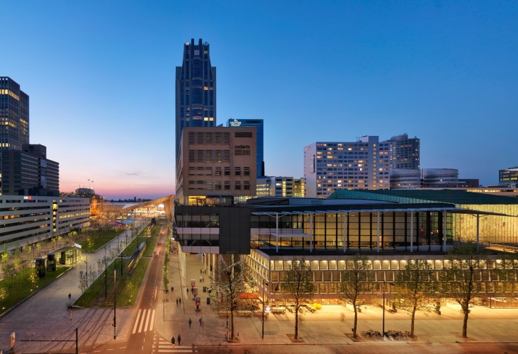 Buitenaanzicht van de Doelen ICC Rotterdam in de avondschemering, gelegen in het centrum van Rotterdam. Het moderne gebouw is zichtbaar in zijn stedelijke context, met omliggende hoogbouw en het Rotterdam Centraal Station op loopafstand op de achtergrond.