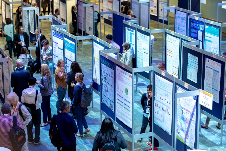 De foto toont de Willem Burger Hal van de Doelen in Rotterdam tijdens een congres. In de ruime hal staan rijen posterpanelen opgesteld met wetenschappelijke presentaties. Bezoekers lopen langs de posters, lezen informatie en gaan met elkaar in gesprek. De hal heeft een open opzet, een stenen vloer en goede verlichting, en is geschikt voor exposities, posterpresentaties, netwerkmomenten en congressen.