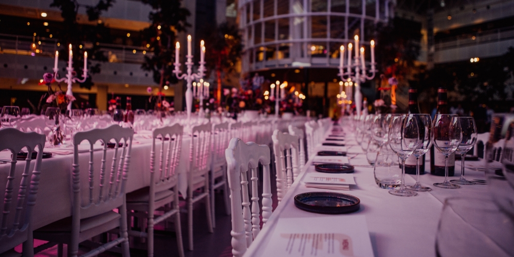 Luxe lange dinertafel met witte stoelen, kaarsen en glaswerk, sfeervol gedekt voor een exclusief diner of evenement.