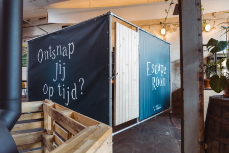 Mobiele escape room voor teambuilding op locatie, ingericht in een industriële ruimte met planten en houten elementen.