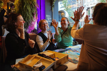 Collega’s vieren een overwinning tijdens een interactieve teambuildingactiviteit op locatie van The Box Company genaamd Connect & Collab, waarbij ze samenwerken aan een creatieve opdracht.