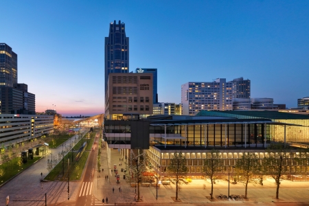 Buitenaanzicht van de Doelen ICC Rotterdam in de avondschemering, gelegen in het centrum van Rotterdam. Het moderne gebouw is zichtbaar in zijn stedelijke context, met omliggende hoogbouw en het Rotterdam Centraal Station op loopafstand op de achtergrond.
