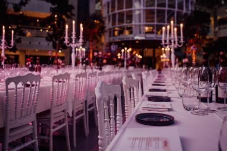 Luxe lange dinertafel met witte stoelen, kaarsen en glaswerk, sfeervol gedekt voor een exclusief diner of evenement.